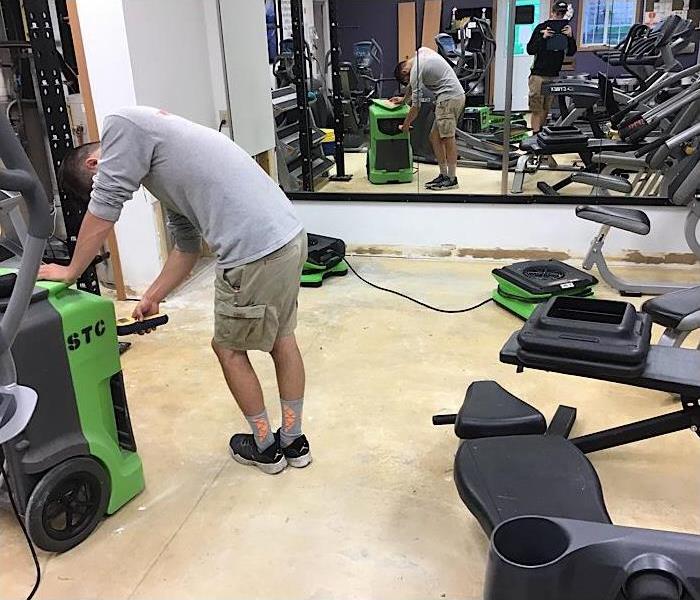 A young man from SERVPRO of St. Cloud taking readings to test the dryness of the area in the workout facility. 